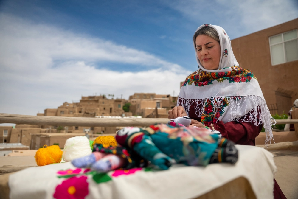 Women carpet weaving with Qaleh Bala in the background